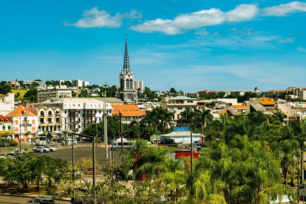Vue panoramique du centre-ville de Fort-de-France en Martinique avec la cathédrale Saint-Louis en arrière-plan et des palmiers au premier plan.